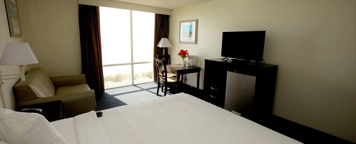 A hotel room with a bed, chair, TV, and window.