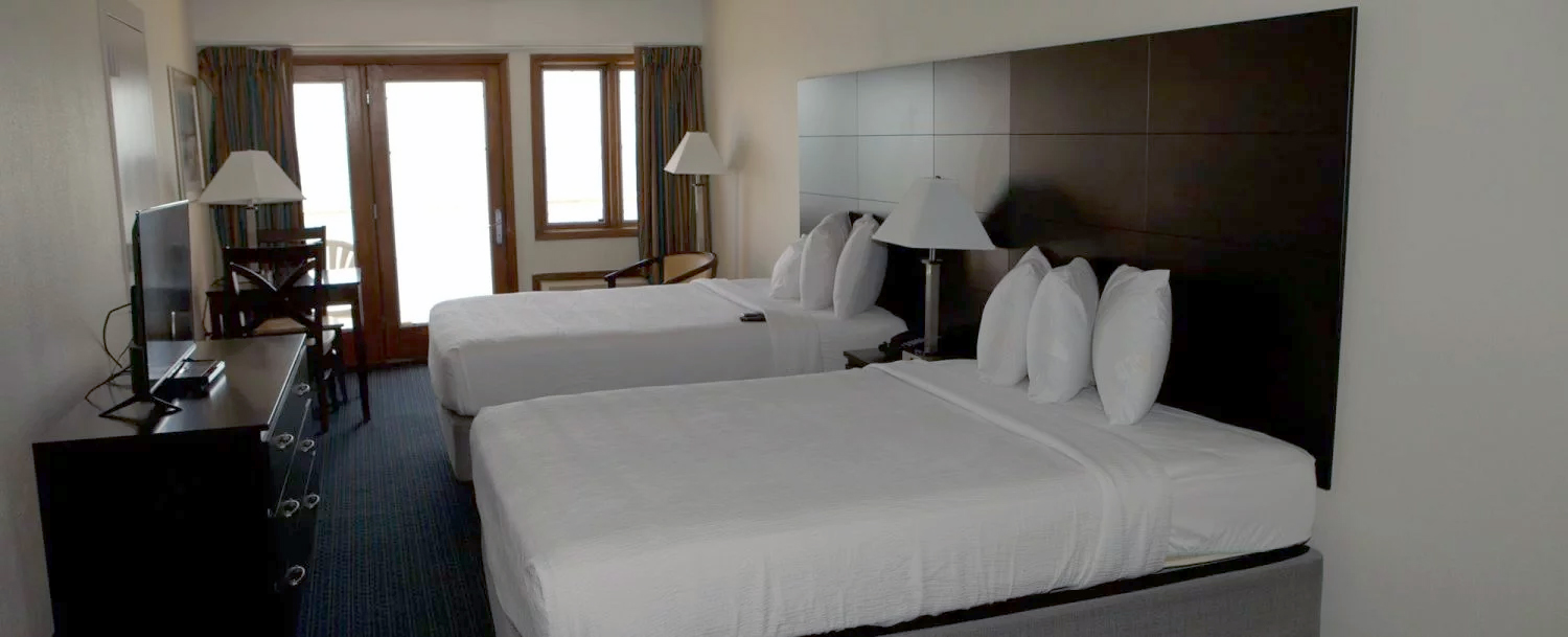 A hotel room with two beds, a desk, a TV, and a doorway leading outside.